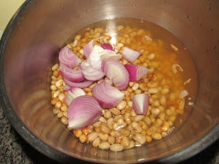 Unpeeled beans and diced onion in a bowl with water for blending